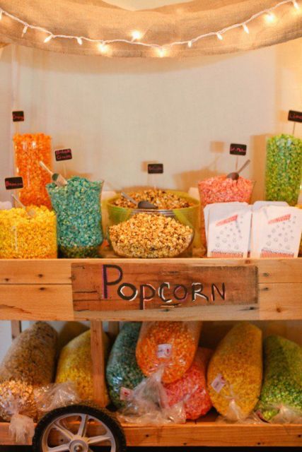 a fun and bright popcorn bar made of a wagon on wheels, with colorful popcorn in glass bowls and in sacks