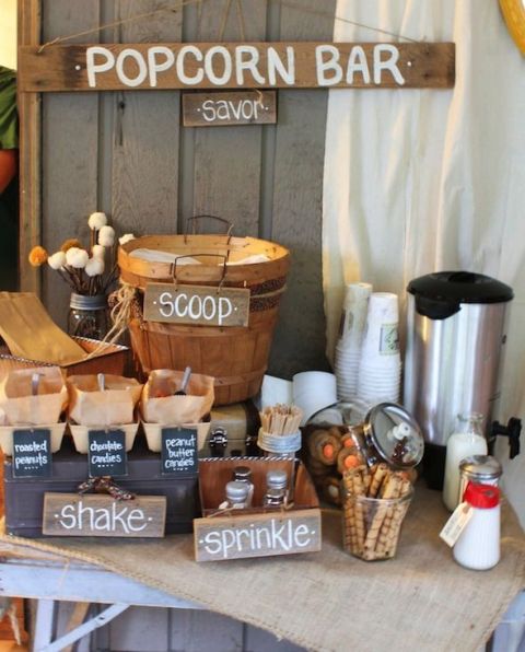 a rustic popcorn bar with wooden signage, boxes, a kettle, cups and a wooden basket with popcorn plus paper bags
