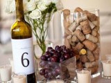 a wedding centerpiece of grapes, wine corks, a wine bottle with a number and white blooms