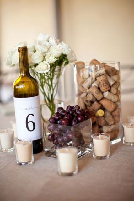 a wedding centerpiece of grapes, wine corks, a wine bottle with a number and white blooms