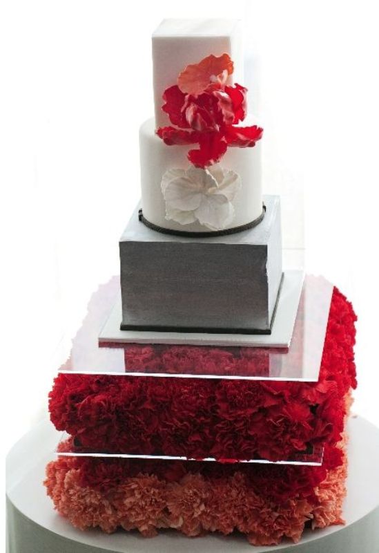 a grey and white wedding cake with white and red sugar blooms served on a pillow of red blooms