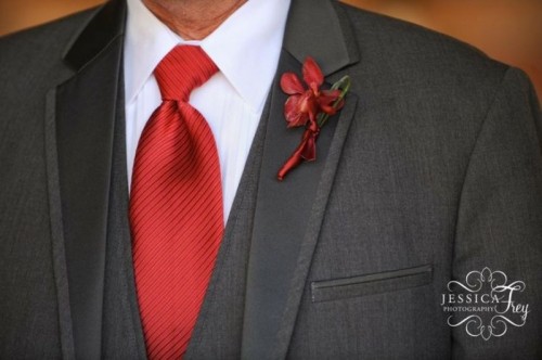 a grey three-piece wedding suit plus a red tie and a red floral boutonniere