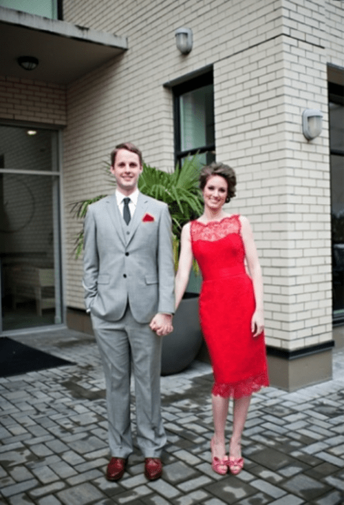 a chic dressed couple - a grey three-piece suit, a grey tie, red shoes and a short red lace dress and red shoes