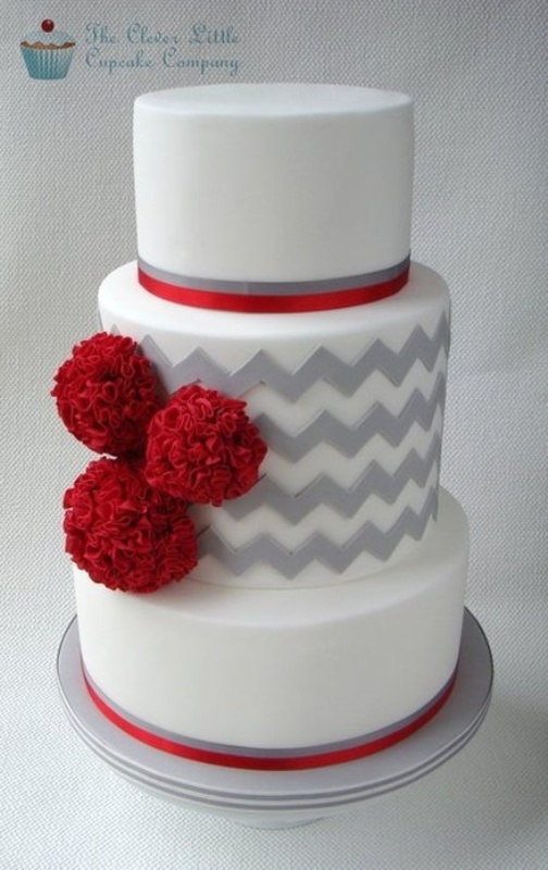 a grey and white wedding cake with chevron patterns, red ribbons and red pompoms