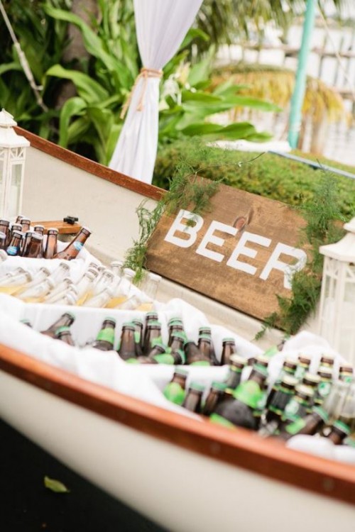 a simple and relaxed wedding bar idea - a boat with greenery, candle lanterns and a sign and lots and lots of beer in boxes with ice is a great idea