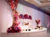 an oversized glam wedding bar of a rounded bar stand clad with white tiles, with a tree covered with colorful blooms and candles is a very refined idea