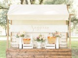 a beautiful wedding drink bar of a planked wooden stand and a roof made of fabric, with beautiful blooms, lemonade and glasses is a very cute and delicate idea