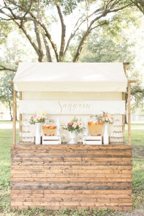 a beautiful wedding drink bar of a planked wooden stand and a roof made of fabric, with beautiful blooms, lemonade and glasses is a very cute and delicate idea