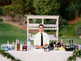 a lovely wedding drink bar – a table with white tablecloth and a greenery garland, an open shelving unit with glasses is a lovely idea to go for