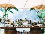 a stylish vineyard wedding drink bar composed of wine barrels and a tabletop, with greenery and white blooms around is chic