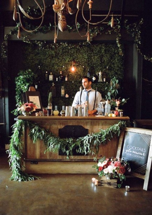 a beautiful wedding bar with a living wall as a backdrop, open shelves, a wooden drink bar with much greenery and lights around is a beautiful and chic idea