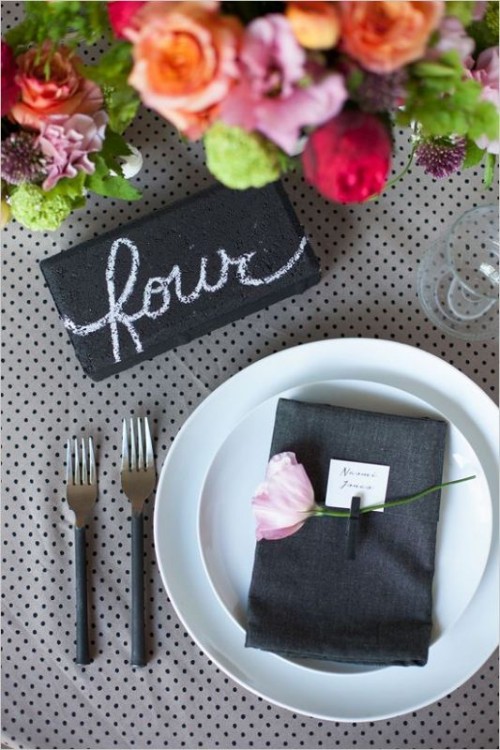 a playful wedding tablescape with a polka dot tablecloth, bright blooms, white plates and a black napkin is cool