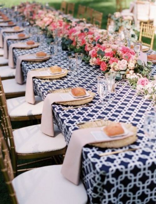a bright summer wedding tablescape with a navy printed tablecloth and neutral napkins, bold pink and blush blooms and gold-rimmed glasses