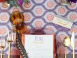 a bright and whimsical wedding tablescape with a bold printed runner, jewel-tone blooms, a bold napkin and an amber glass