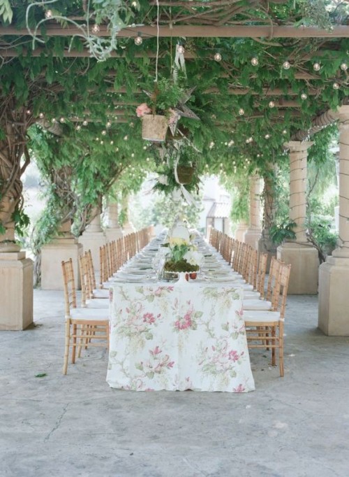 a beautiful garden wedding reception table with a floral print tablecloth, greenery and white blooms and pendant lamps