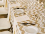a glam chic wedding tablescape with a gold glitter chevron tablecloth, white tableware, white candles and neutral napkins