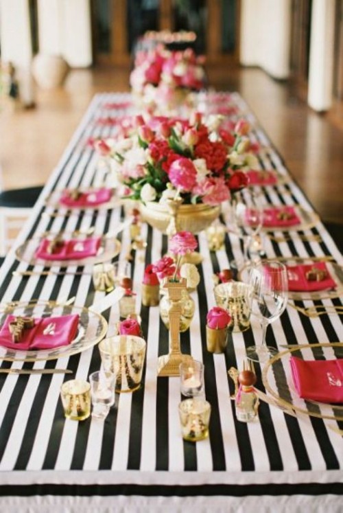 a bright and chic wedding tablescape with a striped tablecloth, fuchsia napkins and blooms, gold candleholders and vases with bold blooms