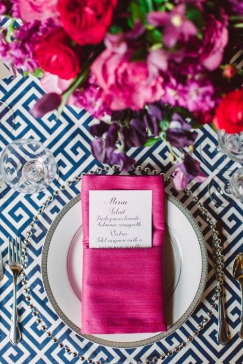 an elegant and chic wedding table setting with a navy printed tablecloth, fuchsia napkins, jewel-tone blooms and silver cutlery