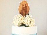 a white wedding cake with a blue ribbon, with white hydrangeas and a wooden and woodburnt cake topper is a lovely and cute idea