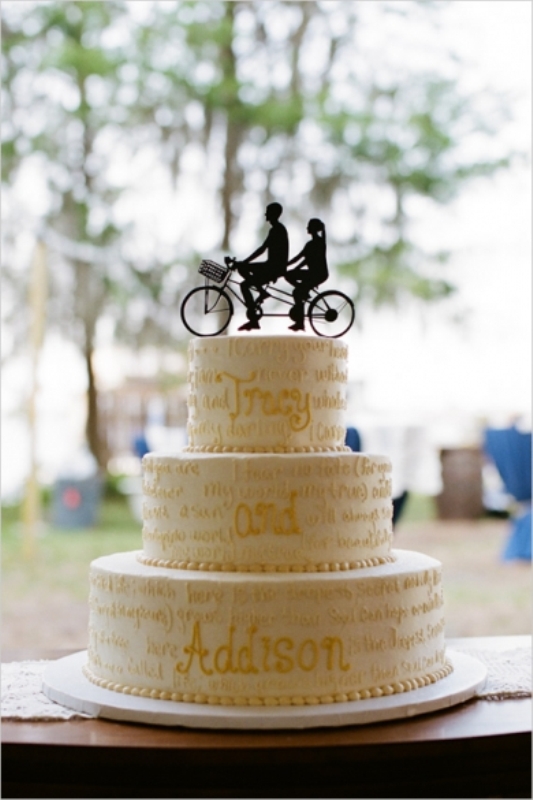 a white calligraphy wedding cake with a black couple and bike silhouette cake topper is great for a couple who loves bikes