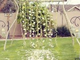 a rustic backyard wedding arch with hanging greenery and white blooms and greenery and blooms right on the ground