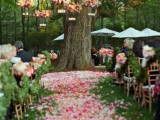 a pretty backyard wedding ceremony space with a living tree decorated with greenery and blooms, with the aisle covered with bright petals and greenery garlands