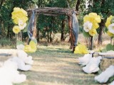 a simple backyard wedding arch decorated with grey fabric, with yellow and white paper blooms and leaves decorating the aisle