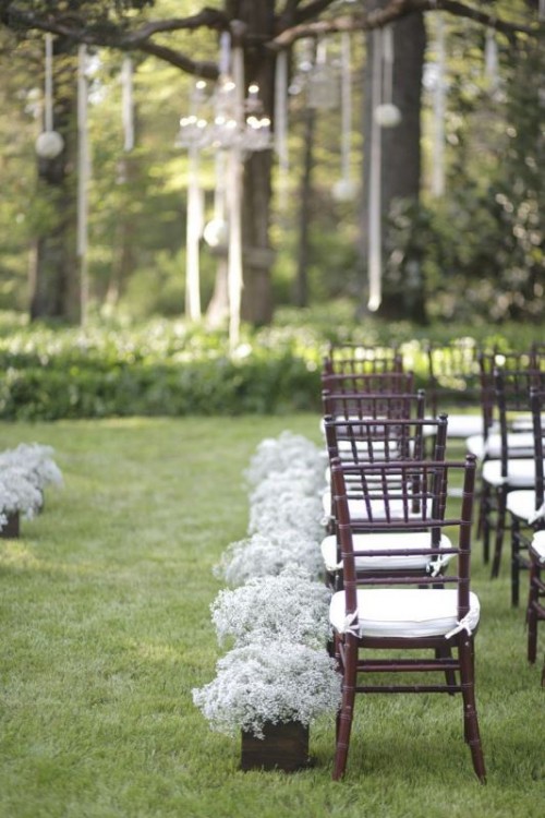 a chic backyard wedding ceremony space with ribbons and baby's breath balls hanging froma  tree, baby's breath in pots along the wedding aisle