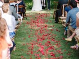 a boho backyard wedding ceremony space with red petals on the ground, a boho wedding arch with macrame is cute and cool