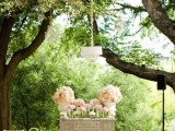 a refined backyard wedding ceremony space with a buffet with blooms, a crystal chandelier hanging over it and an aisle decorated with white hydrangeas