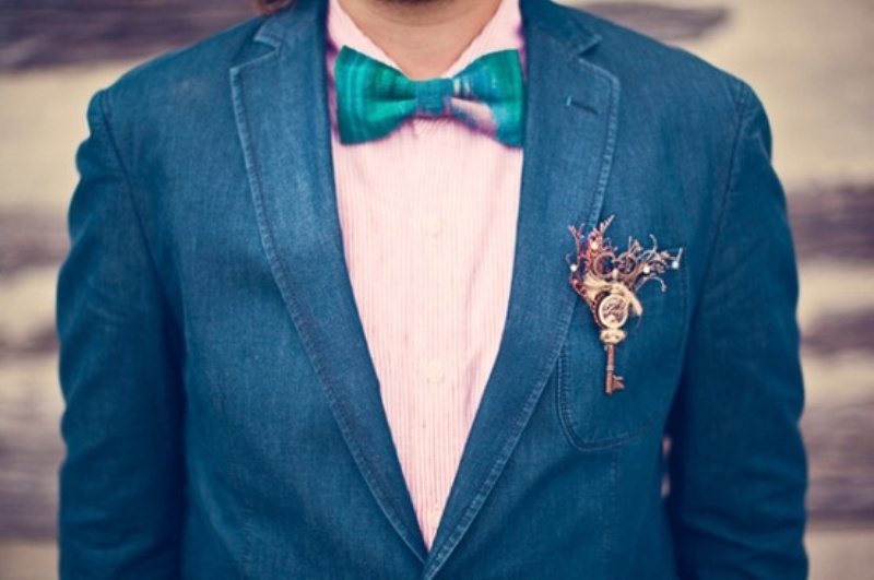 A navy suit, a pink printed shirt, a bright turquoise bow tie and a steampunk boutonniere with a vintage key