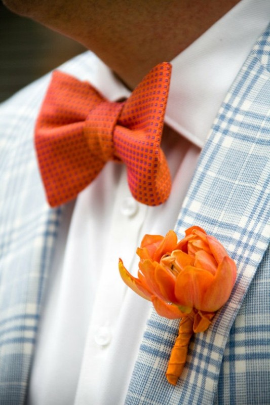 A light blue plaid blazer accented with an orange floral boutonniere and a matching bow tie for a contrast