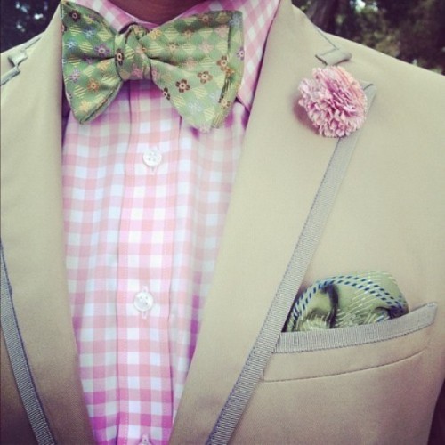 a neutral suit, a plaid pink shirt, a colorful printed bow tie and a green handkerchief for a spring or summer look