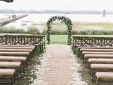 a lovely rustic wedding ceremony space with a burlap path with petals and upholstered benches, plus grass and greenery around