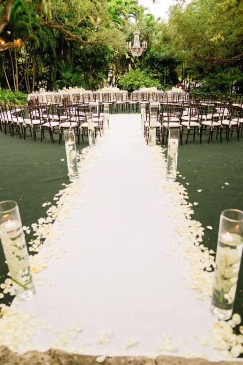 dark-stained chairs with white seats and a white pathway with floating candles and petals on the path