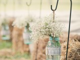 a rustic wedding aisle of hay stacks, metal stands holding blue mason jars, with lace and white baby’s breath is a stylish and cute decor idea