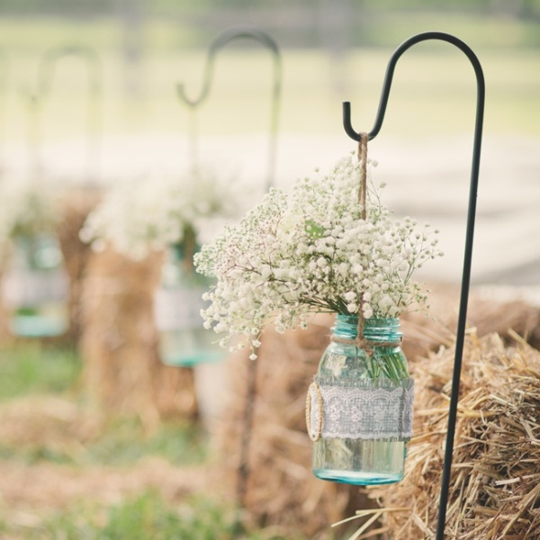 a rustic wedding aisle of hay stacks, metal stands holding blue mason jars, with lace and white baby's breath is a stylish and cute decor idea