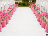 a fun and colorful wedding aisle with a white runner, pink mason jars with matching pink gerberas is a cool idea for a modern wedding
