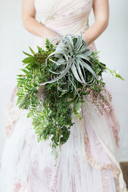 A unique wedding bouquet with textural cascading greenery, some blooming branches and a large air plant