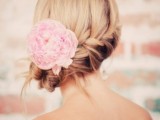 a low wedding updo with a braid and a pink bloom tucked in the hair is a lovely and chic idea for a destination wedding
