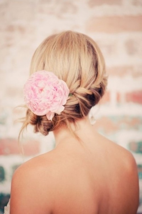 a low wedding updo with a braid and a pink bloom tucked in the hair is a lovely and chic idea for a destination wedding