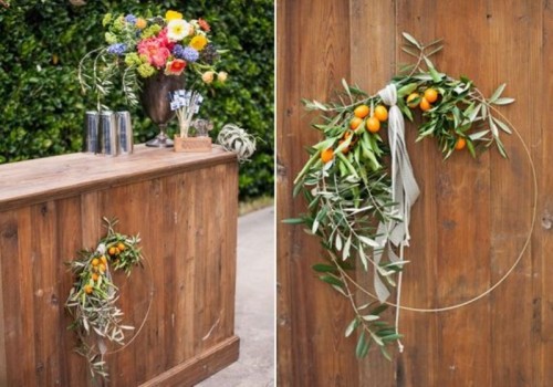 a round wedding wreath of metal, with greenery and kumquats and ribbons is a pretty and bright decor idea for a wedding in summer