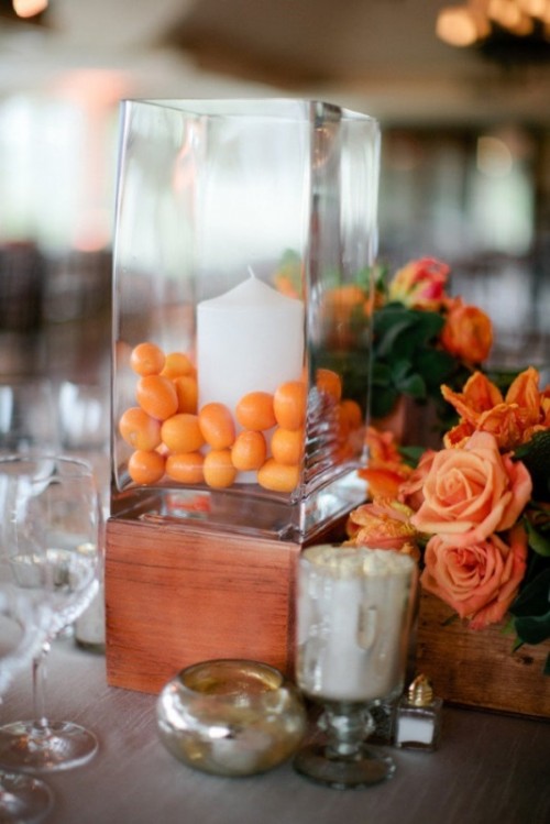 a bold wedding centerpiece of orange roses and greenery, a box with a pillar candle and some kumquats is a bright and cool idea