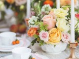 a pastel wedding centerpiece with yellow, pink, orange and white blooms, thin and tall candles and white porcelain with kumquats