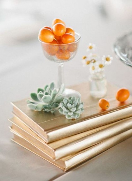 pretty wedding decor with gold books, succulents, kumquats and a glass with this kind of fruit is a very chic idea