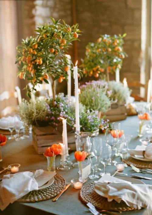 a lovely wedding tablescape done with woven placemats, orange tulips and kumquat trees in crates placed on the table as centerpieces, potted greenery