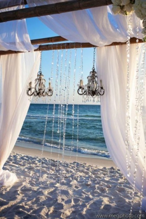 a beach wedding arch with crystals, crystal chandeliers and light and flowy curtains for a breezy look