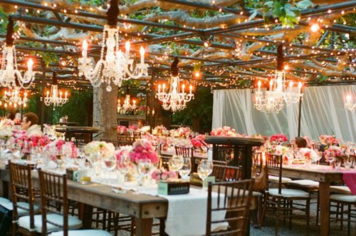 a bright wedding reception outdoors with bright blooms and crystal chandeliers hanging over the space is amazing