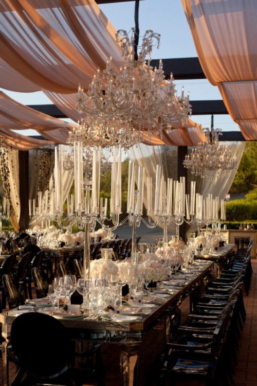 a super exquisite wedding reception space with tall candelabras, white blooms and crystal chandeliers over the space is amazing