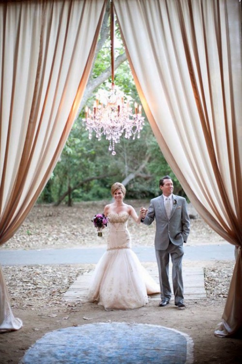a wedding ceremony space with neutral curtains and a chic crystal chandelier that illuminates and accents the space